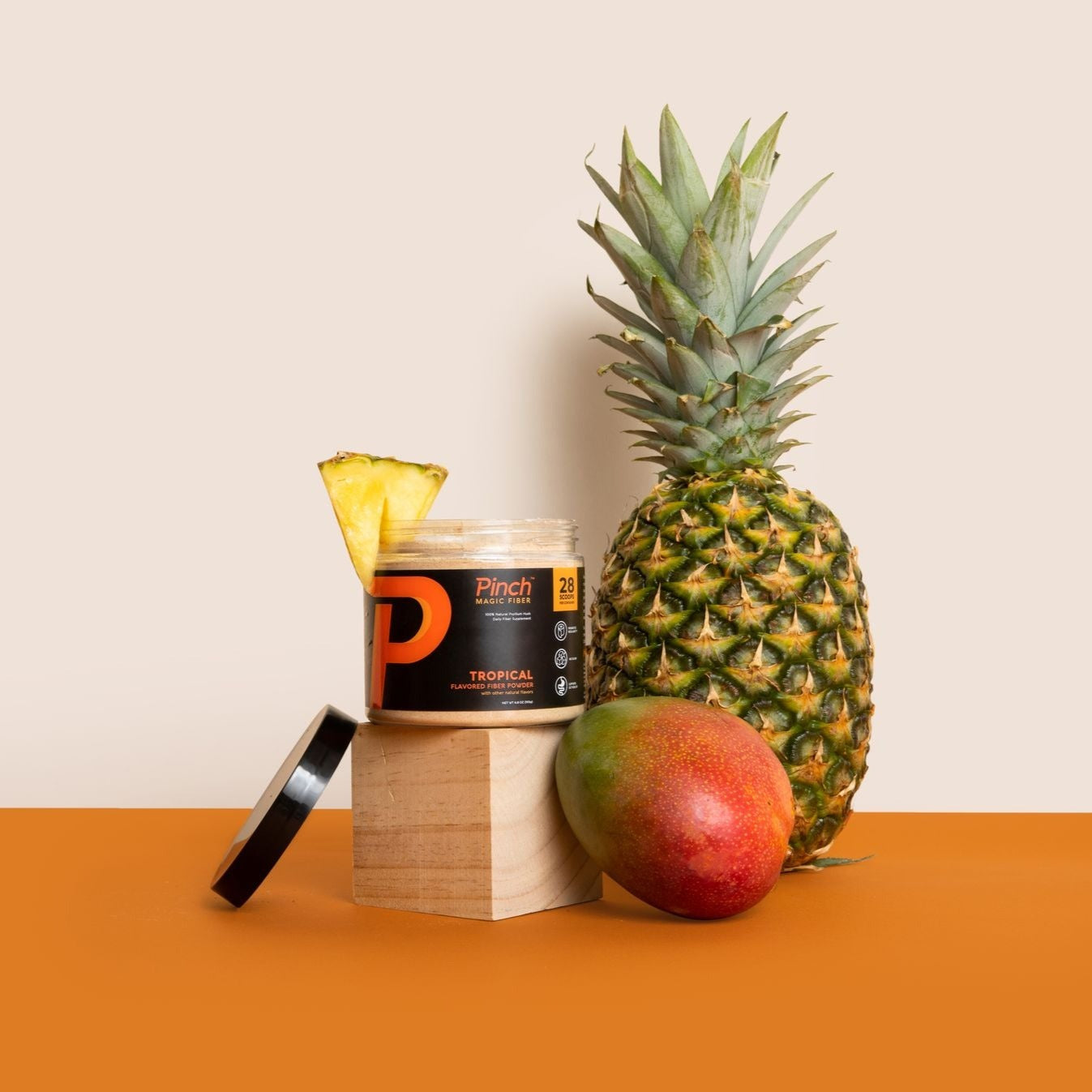 Pinch Magic Fiber jar with pineapple and mango on an orange surface.